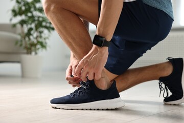Man tying shoelace of sneaker indoors, closeup