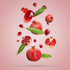 Fresh pomegranates, seeds and leaves in air on light red background