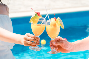 バカンス・リゾートホテルのプールサイドでトロピカルドリンクで乾杯するカップルの手元  © buritora