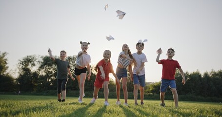 Group of Children Tossing Paper Airplanes in the Park at Dusk, Embracing Summer Fun, Slow Motion