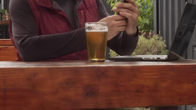 Hombre trabajando en laptop con cerveza artesanal en bar exterior