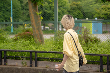 Fototapeta premium In early summer, a Japanese man in his twenties wearing yellow clothes, walking and strolling through Yoyogi Park, Shibuya, Tokyo, during the day.