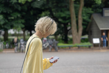 Fototapeta premium In early summer, a Japanese man in his twenties wearing yellow clothes, walking and strolling through Yoyogi Park, Shibuya, Tokyo, during the day.