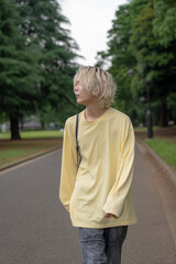 In early summer, a Japanese man in his twenties wearing yellow clothes, walking and strolling through Yoyogi Park, Shibuya, Tokyo, during the day.