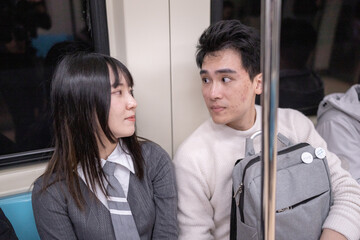 A Taiwanese woman in her twenties and a Hong Kong man are riding the subway in Taipei City, Taiwan, chatting and using a smartphone.