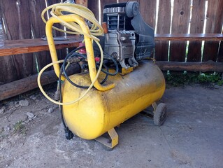 A yellow compressor stands in a gazebo in the yard. Electric tool for creating pressure.