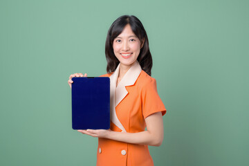 A young woman in an orange dress with white accents stands against a green background, holding up a...
