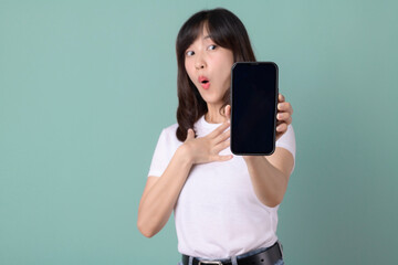 Woman in a white t-shirt pointing at a smartphone with an excited expression on a green background, expressing enthusiasm.