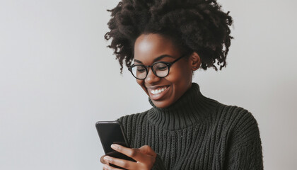 Smiling woman with curly hair and glasses looking at her phone against a white background