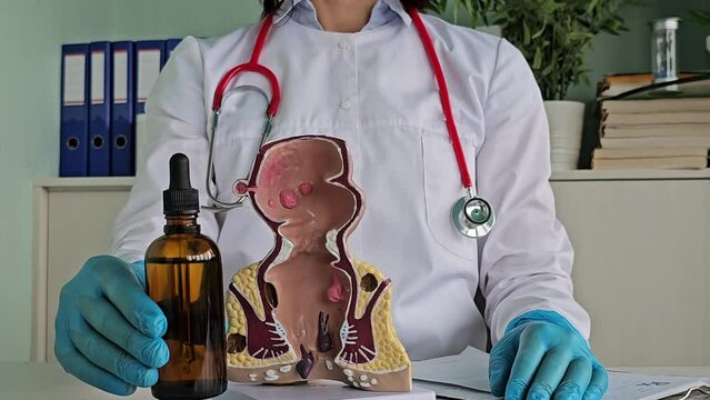 Proctologist holds Vaseline oil for constipation in the rectum. Anatomical model of rectum with hemorrhoids