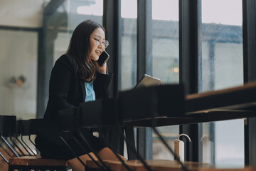 Asian woman entrepreneur busy with her work in the office. Young Asian woman talking over phone or cellphone while sitting at her desk.