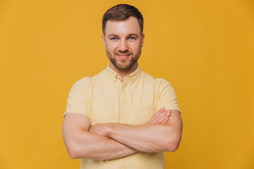Cute unshaven man smiling with healthy teeth and crossed arms in yellow shirt posing isolated on yellow background with copy space