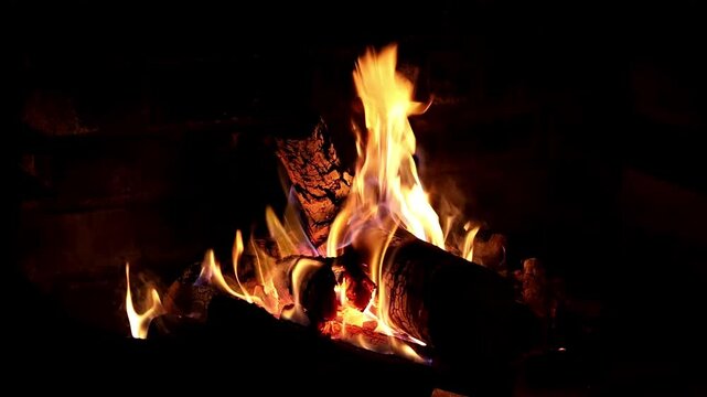 Warm wood crackling fireplace with glowing flames in slow motion - tranquil outdoor dark evening