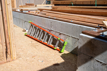 New home construction detail, ladder leaning against cement foundation with wood sill plate and anchor bolts, stack of delivered lumber ready for framing, sunny day job site  © knelson20