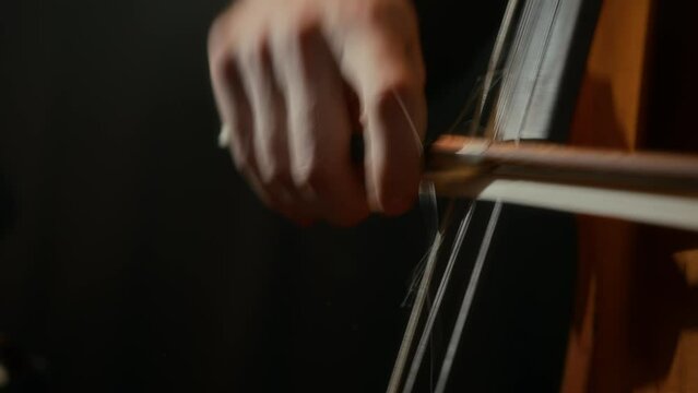 Closeup of unrecognizable male cellist playing his instrument virtuously on black background
