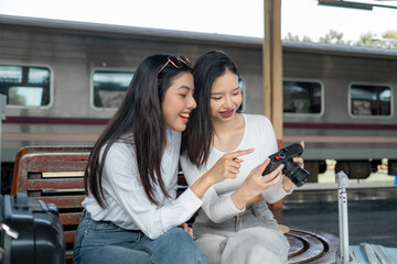Smiling women on the station platform with happily looking into a smartphone, girls standing at train station take selfie photo on smartphone
