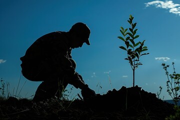 Naklejka premium Silhouette of an environmental resource officer planting a young tree in a reforestation project. The background showcases a lush green landscape, indicating the positive impact of their work. The