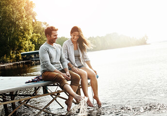 Vacation, couple and sitting on dock in nature for holiday, fun and splashing feet in water in summer. Happiness, people and romantic getaway by lake for adventure, commitment or love in relationship