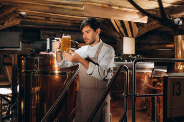 Bearded male brewer sipping delicious ber from a glass, working at his production brewery. Professional brewer tasting fresh beer at his microbrewery, drinking with his eyes closed. Pleasure concept