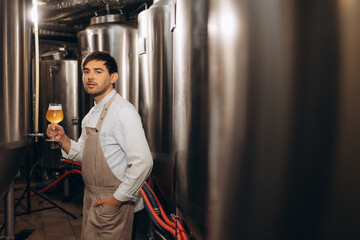 young bearded attractive male brewer with wooden beer mug in hand on background of brewery