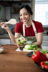 Image of young asian woman in apron preparing salad or food in the kitchen at home.