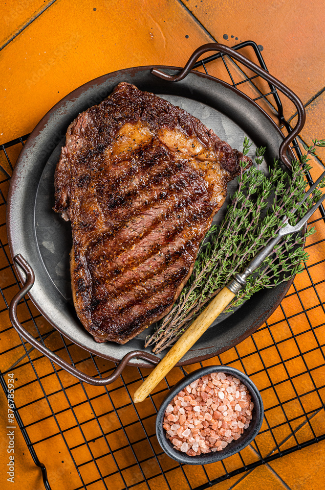 Wall mural bbq grilled wagyu rib eye beef meat steak with herbs in steel tray. orange background. top view