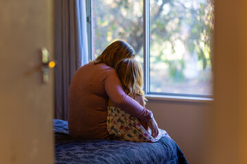 view through a partly open door to a dark bedroom where a mother is comforting her young daughter