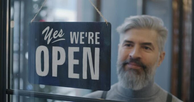 Close-up of mature man waiter hanging Open sign on cafe door waiting for client developing catering business. People and start-up concept.