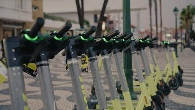 A row of electric scooters lined up on a city street, ready for convenient urban transportation. The scooters are parked in a well-organized manner, promoting eco-friendly travel in the city.