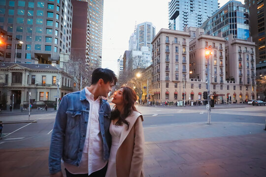Engaged couple embracing in the city with focus on Melbourne cityscape in background at night