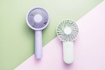 Small portable mini fans on green and pink background close-up.