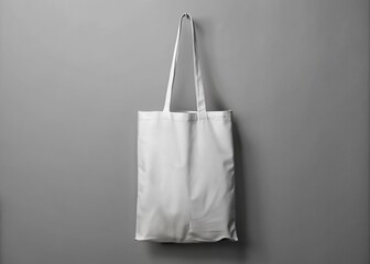 Isolated white tote bag mockup suspended from a metal hook on a clean gray background, awaiting custom design or branding with plenty of negative space.