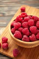 Raspberries in wooden bowl on brown background. Vertical photo