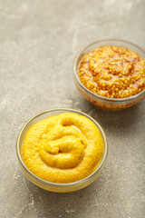 Dijon mustard with french mustard on grey concrete background. Vertical photo