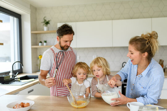 Young nuclear family making pancakes together. Parents and children in kitchen, preparing pancake batter, spending weekend day indoors.