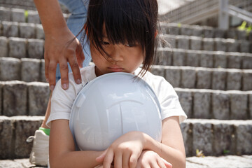 落ち込んでいる小学生と肩をたたいて慰める人の手