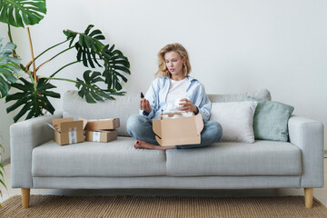 Young woman examining products sitting on sofa at home