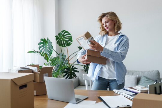 Freelancer reading details on delivery boxes standing at home office
