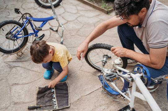 Father repairing son's bicycle crouching on floor