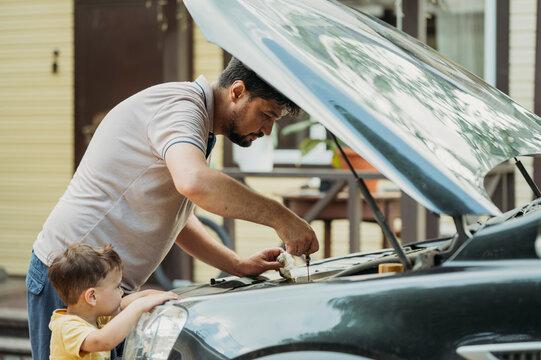 Father checking oil level standing with son near car