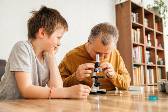 Man looking through microscope and sitting with son at home