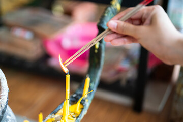 Action of a human hand is igniting incense stick for make a worship at Buddha temple. Religion and culture scene, close-up and selective focus.
