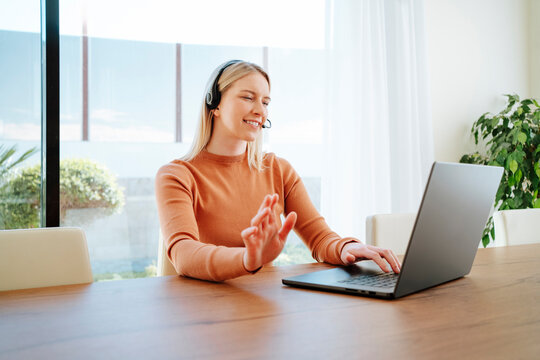 Smiling young businesswoman with headset working on laptop at table