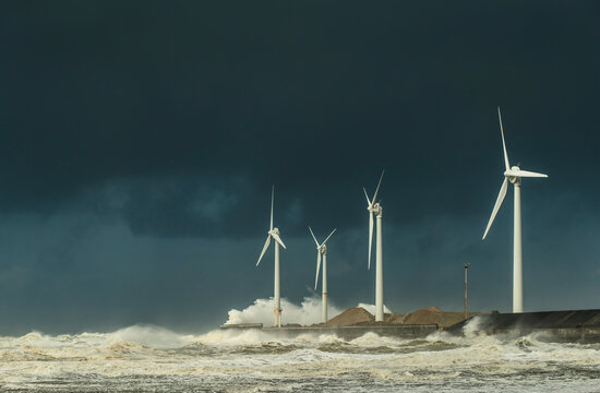 Waves breaking near wind turbines on coastline under cloudy sky