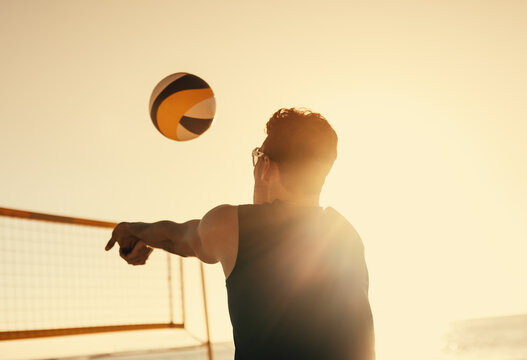 Pro beach volleyball player spiking ball at sunset on the coastal beach