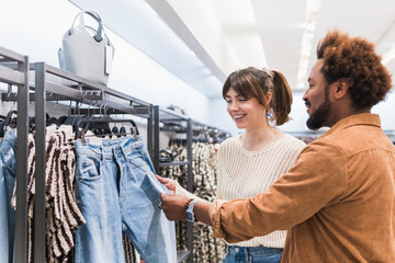 Smiling couple examining denim jeans on display in shopping mall