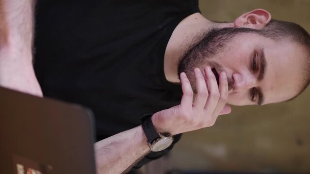 A young man with light beard stubble works on his computer in a vertical clip but then yawns from boredom, showing signs of fatigue and disinterest