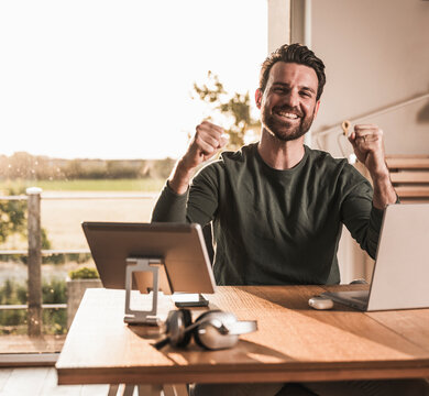 Happy freelancer gesturing and cheering at desk in home office