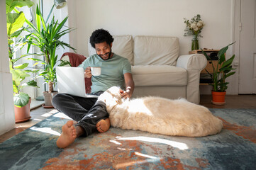 Smiling freelancer holding tea cup and sitting with dog in living room at home