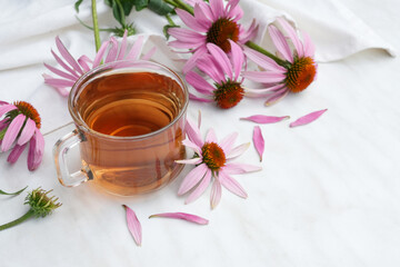 Herbal tea in a glass cup, flowers echinacea, napkin on a white marble table. Side view. Space for text. 